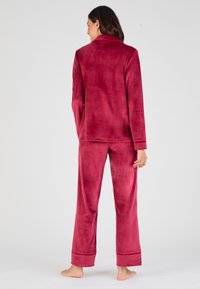 Conjunto de pijama de felpa carmesí que incluye una camiseta de manga larga con cuello y pantalones de pierna ancha. Textura suave y corte holgado.