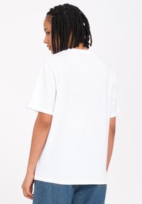 Weißes Baumwoll-T-Shirt mit kurzen Ärmeln, Rundhalsausschnitt und lockerer Passform. Der Rücken ist schlicht und ohne Grafiken oder Muster.