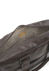 Bolso mensajero de cuero marrón con apertura con cremallera. El interior cuenta con un forro estampado y una pequeña etiqueta de logo. Incluye correa ajustable.