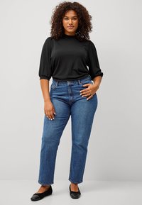 Zwarte top met pofmouwen, gecombineerd met hoogtaille blauwe denim jeans. Zacht materiaal met een gladde textuur; klassiek ontwerp en recht gesneden pijpen.