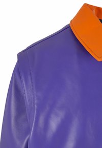 Fialová kožená bunda s lesklým povrchem, která má oranžový, lesklý límec. Detail ukazuje šev na rameni a texturu materiálu.