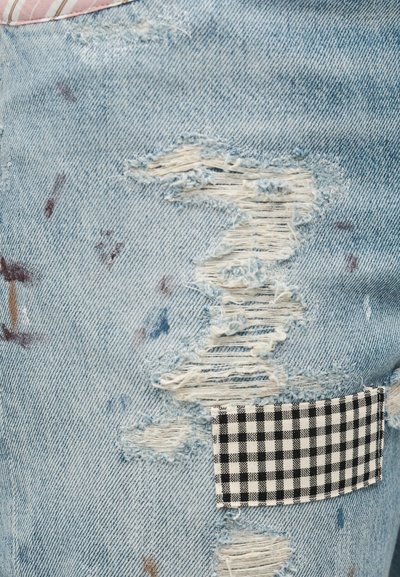 Ανοιχτό μπλε φθαρμένο τζιν με μεγάλες τρύπες και μια ασπρόμαυρη καρό υφασμάτινη επιδιόρθωση ραμμένη στην περιοχή του μηρού.
