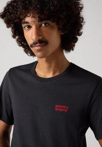 Svart bomull T-skjorte med en liten rød Levi's-logo på venstre bryst, med en klassisk rund halslinning og glatt tekstur.
