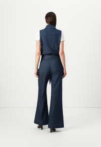 Denim jumpsuit met een getailleerde taille, wijde broekspijpen en een mouwloze kraagtop, met een donkerblauwe wassing en minimale stikseldetails.