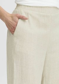 Beige linnen broek met een gestructureerde afwerking, voorzien van een zijzak, elastische taille en een ontspannen pasvorm.