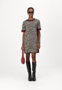 Leopardenmusterkleid mit kurzen Ärmeln, roten gestreiften Akzenten und geradem Schnitt. Kombiniert mit kniehohen schwarzen Stiefeln und einer roten Tasche.