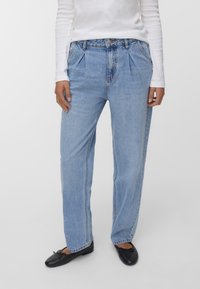 Světle modré denimové džíny s vysokým pasem, sklady na přední straně, uvolněný střih a rovné nohavice. V kombinaci s černými plochými botami.