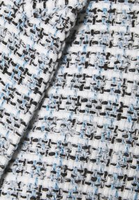 Detailní záběr na tkaninu s bílými, černými a světle modrými niti v texturovaném, mřížkovém vzoru.