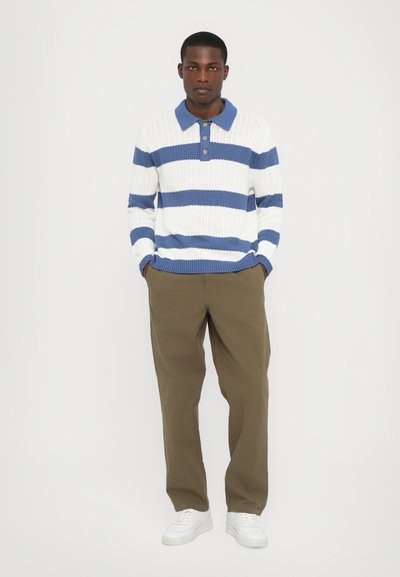 Hvit og blå stripete strikket polo genser med blå krage, tre knapper, parret med olivengrønne bukser og hvite sneakers.
