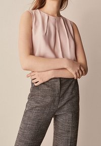 Helle rosa ärmellose Bluse mit gefaltetem Vorderdesign, kombiniert mit grauen Hosen mit Karomuster und hoher Taille. Glatte Textur und figurbetonter Schnitt.