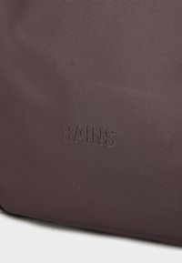 Tmavohnedá vodotesná taška s hladkým povrchom, s embosovaným logom "RAINS", minimalistický dizajn a bez viditeľného kovania.