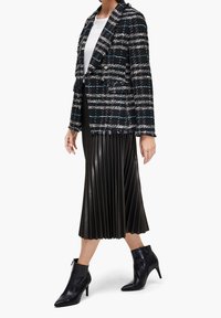 Blazer de tweed negro y blanco de doble botonadura, con acentos azules, combinado con una falda plisada de piel sintética negra y botines de tacón alto negros.