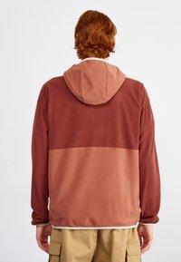 Felpa con cappuccio bicolore in bordeaux e terracotta, realizzata in morbido tessuto con una vestibilità comoda. Include una tasca a marsupio e polsini a costine.
