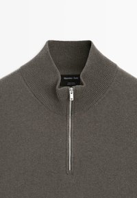 Närmre foto av en grå ulltröja med ribbad hög krage och silvrig halvdragkedja, som visar Massimo Dutti-märket etikett inuti kragen.