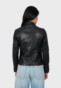 Black leather jacket with a fitted design, notched collar, and visible stitching details, paired with light blue high-waisted jeans.