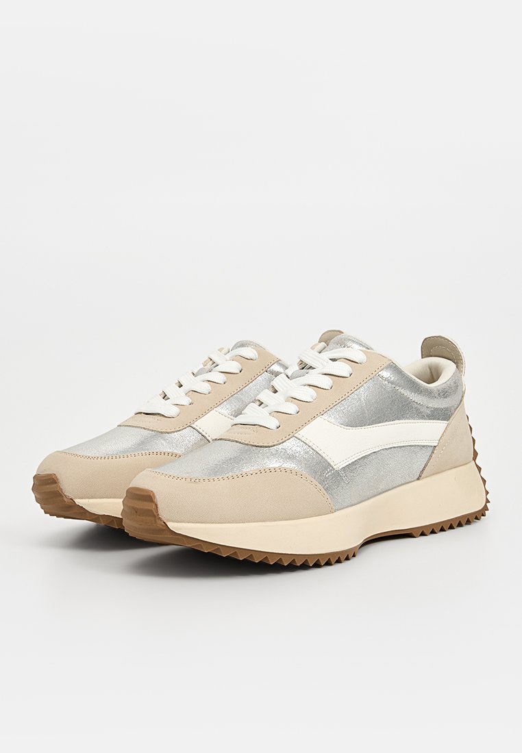 Scarpe da ginnastica beige e argento con una parte superiore texturizzata, accenti bianchi e suola in gomma a zigzag. Presentano lacci e un colletto imbottito.