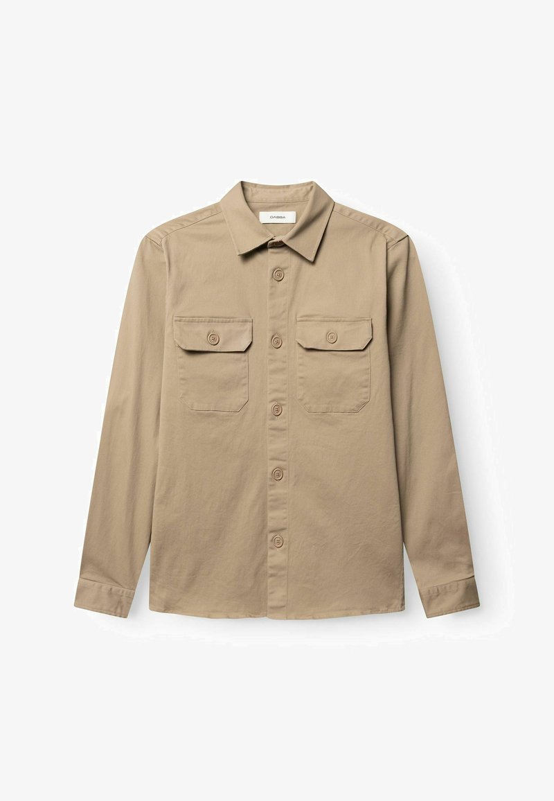 Chemise beige à manches longues avec boutons, dotée de deux poches poitrine boutonnées et d'un col classique, posée à plat sur un fond blanc.