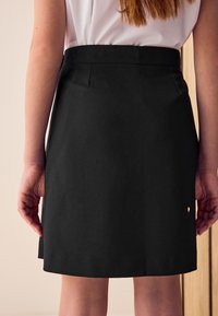 Sort nederdel med en tætsiddende talje, sidelommer og lige snit. Stoffet ser glat ud med en ren kant.