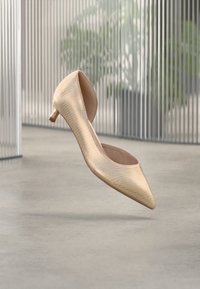 Μπεζ γόβα με μυτερή μύτη και υφή από ψεύτικο δέρμα, με ψηλό, λεπτό τακούνι και ανοιχτή πίσω σχεδίαση.