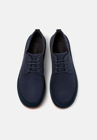 Navy blue canvas shoes with a textured upper, lace-up design, and contrasting rubber sole. Features a round toe and cushioned interior.