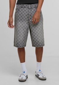 Graue Jeansshorts mit einem strukturierten Kreis-Muster, fünf Taschen und einem Knopfverschluss. Getragen mit weißen Socken und Schuhen.