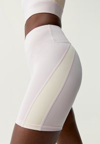 Ljusrosa högmidjade cykelshorts, tillverkade av ett glatt tyg med en krämfärgad sidopanel och platta sömmar som ger en stilren design.