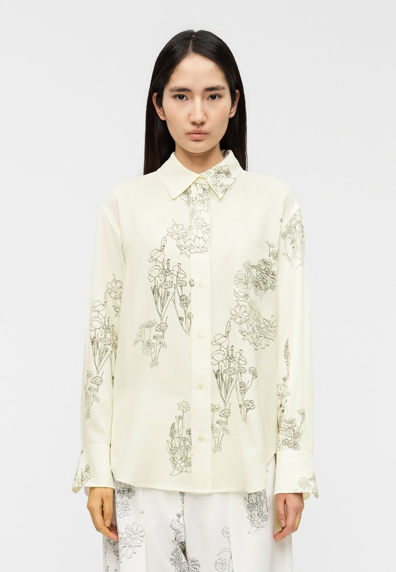 Ελαφριά κρεμ πουκάμισο με κουμπιά, με μαύρα λουλουδένια σχέδια σε γραμμή, με μυτερό γιακά και μακριά μανίκια, διαθέτει τσέπη στο στήθος και χαλαρή εφαρμογή.