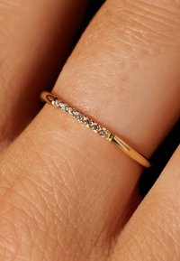 Gouden ring met een rij kleine, heldere edelstenen gezet in een dunne band, getoond op een vinger tegen een neutrale achtergrond.