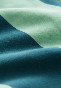 Material cu dungi în nuanțe de teal și verde deschis, tricot texturat cu cusături vizibile, prezentând plisuri și contururi delicate.