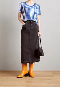 Top de manga corta a rayas azules y blancas, falda midi de denim negra, botas altas brillantes naranjas hasta la rodilla y un pequeño bolso negro con asa.