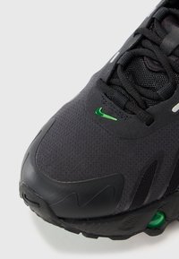 Baskets de sport noires avec un dessus en mesh respirant, un swoosh Nike vert, des accents texturés et une semelle rembourrée pour le soutien et le confort.
