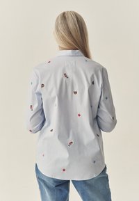 Jasnoniebieska koszula zapinana na guziki z wielokolorowymi haftowanymi wzorami, w tym niedźwiedziami i liśćmi, oraz klasycznym kołnierzem.