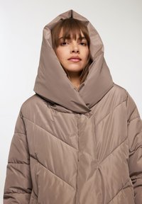 Kurtka puchowa w kolorze taupe z dużym, usztywnionym kapturem. Posiada pikowanie w zygzak oraz gładką, błyszczącą teksturę. Prosty, funkcjonalny design.