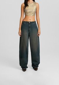 Lesklý zlatý crop top s kulatým výstřihem, spárovaný s volnými tmavými džíny z denimu s vybledlým efektem a vysokým pasem.