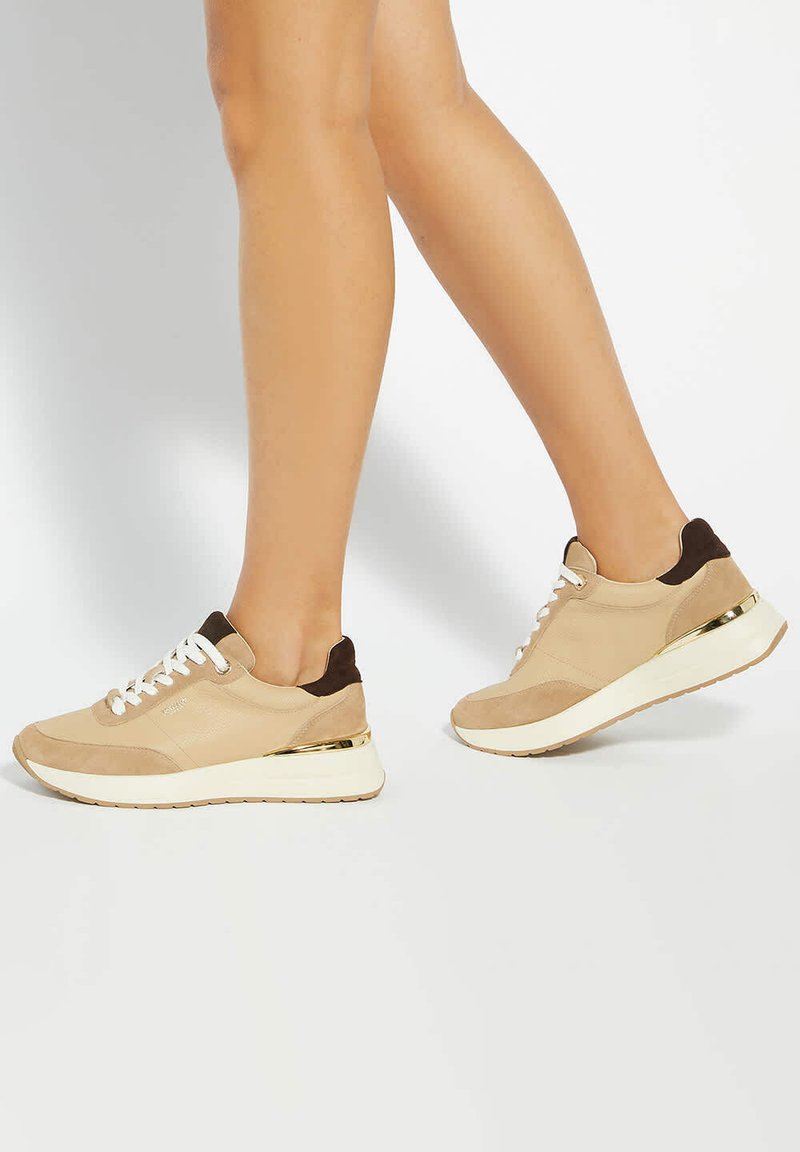Baskets beiges en cuir suédé et mesh, avec une semelle blanche, des accents marron, des détails dorés au niveau du talon et des lacets.