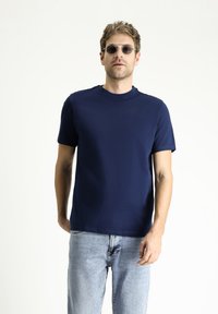 Granatowa koszulka z krótkim rękawem z gładkiego materiału z okrągłym dekoltem, w połączeniu z jasnoniebieskimi dżinsami. Obecne subtelne detale przeszycia.