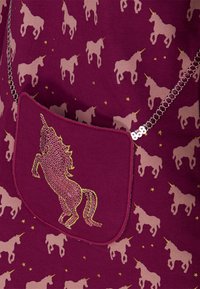 Bordó látka s opakujícími se vzory jednorožců v světle růžové barvě, zdobená kapsa s lesklým zlatým designem jednorožce, stříbrný řetězový detail.