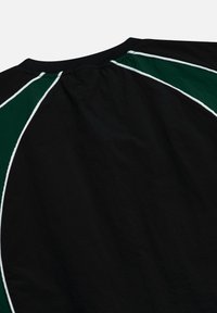 Zwarte top met korte mouwen en een ronde hals. Heeft groene en witte diagonale accenten op de schouders. Glad en licht van stof.