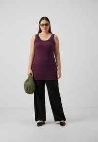 Top in magenta a costine con rifiniture in pizzo, abbinato a pantaloni neri a gamba larga. Porta una borsa trapuntata verde. Scarpe nere flat completano l'outfit.