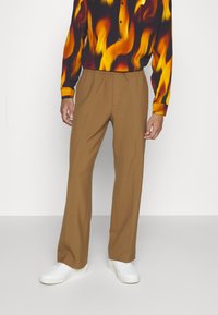 Hnědé, lehké, rovné kalhoty s elastickým pasem, spárované s bílými teniskami a košilí se vzorem plamenů.
