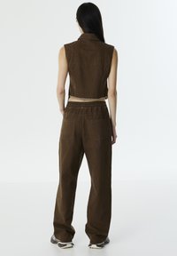 Brązowy denimsowy top bez rękawów o kroju crop, w połączeniu z luźnymi brązowymi spodniami z elastyczną talią i tylnymi kieszeniami.