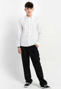 Biała koszula z długim rękawem, zestawiona z luźnymi czarnymi spodniami i czarnymi sneakersami. Koszula ma gładką fakturę i klasyczny krój.