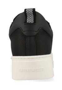 Zapatilla negra con parte superior texturizada y suela blanca. Cuenta con una lengüeta de espiga en la parte trasera y un logotipo en relieve en el talón.