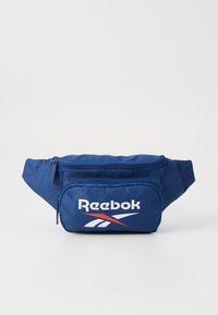 Mochila de cintura em tecido azul marinho com um compartimento principal com fecho e um pequeno bolso frontal com fecho, apresentando um logo da Reebok em branco e detalhes em vermelho.