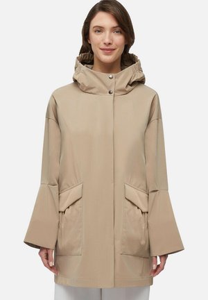 Beige waterdichte jas met een capuchon, grote voorzakken, ruime mouwen en drukknoopsluiting. Soepele textuur en minimalistisch ontwerp.