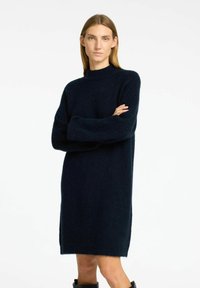 Adīta vilnas kleita tumši zilā krāsā ar augstu kakla izgriezumu, garām piedurknēm un brīvu siluetu. Ievērojamā mīksta, teksturēta apdare.