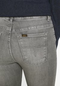 I jeans in denim grigio presentano un classico design a cinque tasche con una piccola etichetta nera e dorata "Lois" sopra la tasca posteriore destra.