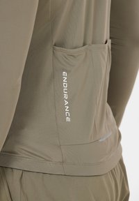 Nahaufnahme einer Tasche aus khakifarbener Sportbekleidung mit vertikal in weißen Buchstaben aufgedrucktem Schriftzug "ENDURANCE".