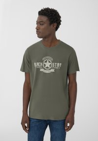 T-shirt verde oliva in cotone, con una grafica che presenta una stella e il testo "BLACK STAR" in stile vintage. Maniche corte, collo rotondo.