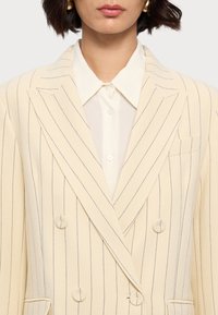 Wendejacke in Off-White mit schmalen blauen Streifen. Mit Reverskragen, zwei Knöpfen und einer Brusttasche. Klassisches Design.